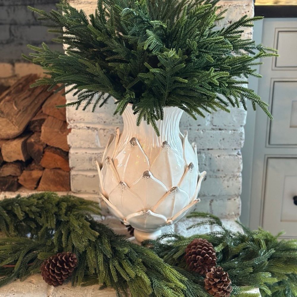 Decorative arrangement with a Scavo artichoke inspired vase, greenery, and pinecones in front of a fireplace.