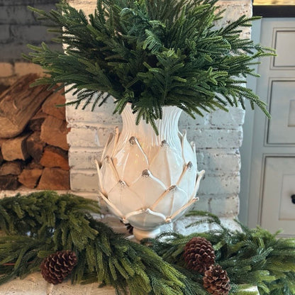 Decorative arrangement with a Scavo artichoke inspired vase, greenery, and pinecones in front of a fireplace.