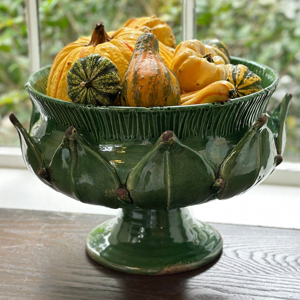 Green ceramic artichoke footed bowl filled with gourds on a wooden surface
