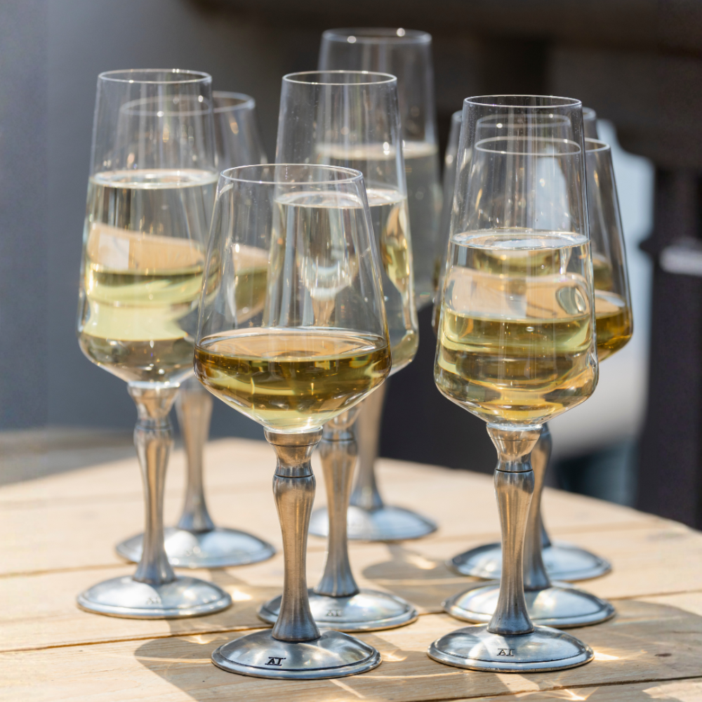 A grouping of Siena pewter based wine and flute glasses with white wine close up on a wooden table