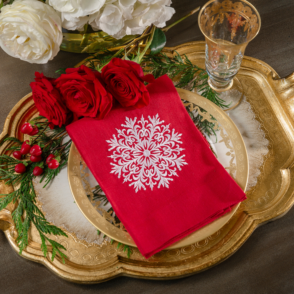 A red Snowflake lane embroidered linen towel folded on a gold tray with roses and a vetro gold flute glass