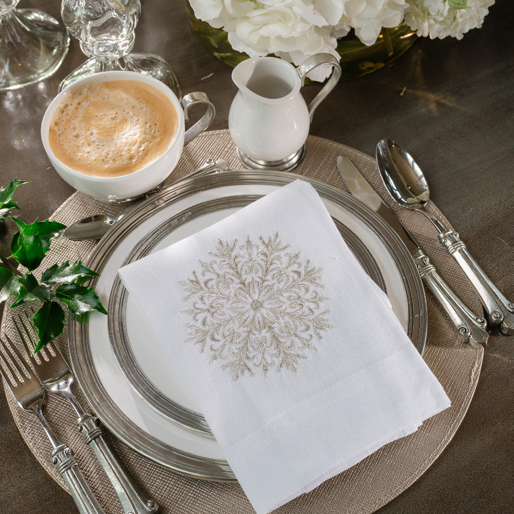 A Tuscan dinnerware place setting with a white embroidered towel with a Snowflake and coffee cup