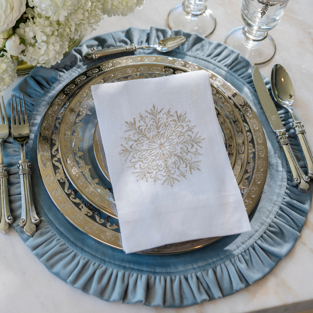 Elegant place setting with Vetro Platinum plates on a light blue velvet placemat with a white linen snowflake lane towel folded on it