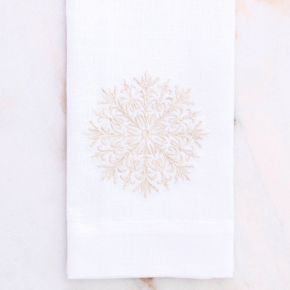White linen towel with champagne embroidered snowflake design on a marble surface