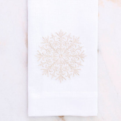 White linen towel with champagne embroidered snowflake design on a marble surface