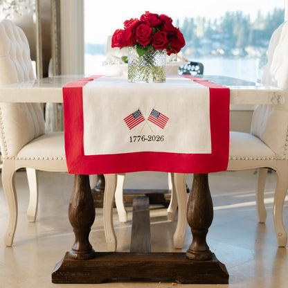 Dining table with a red and white tablecloth featuring embroidered flags and text, set against a blurred outdoor background.