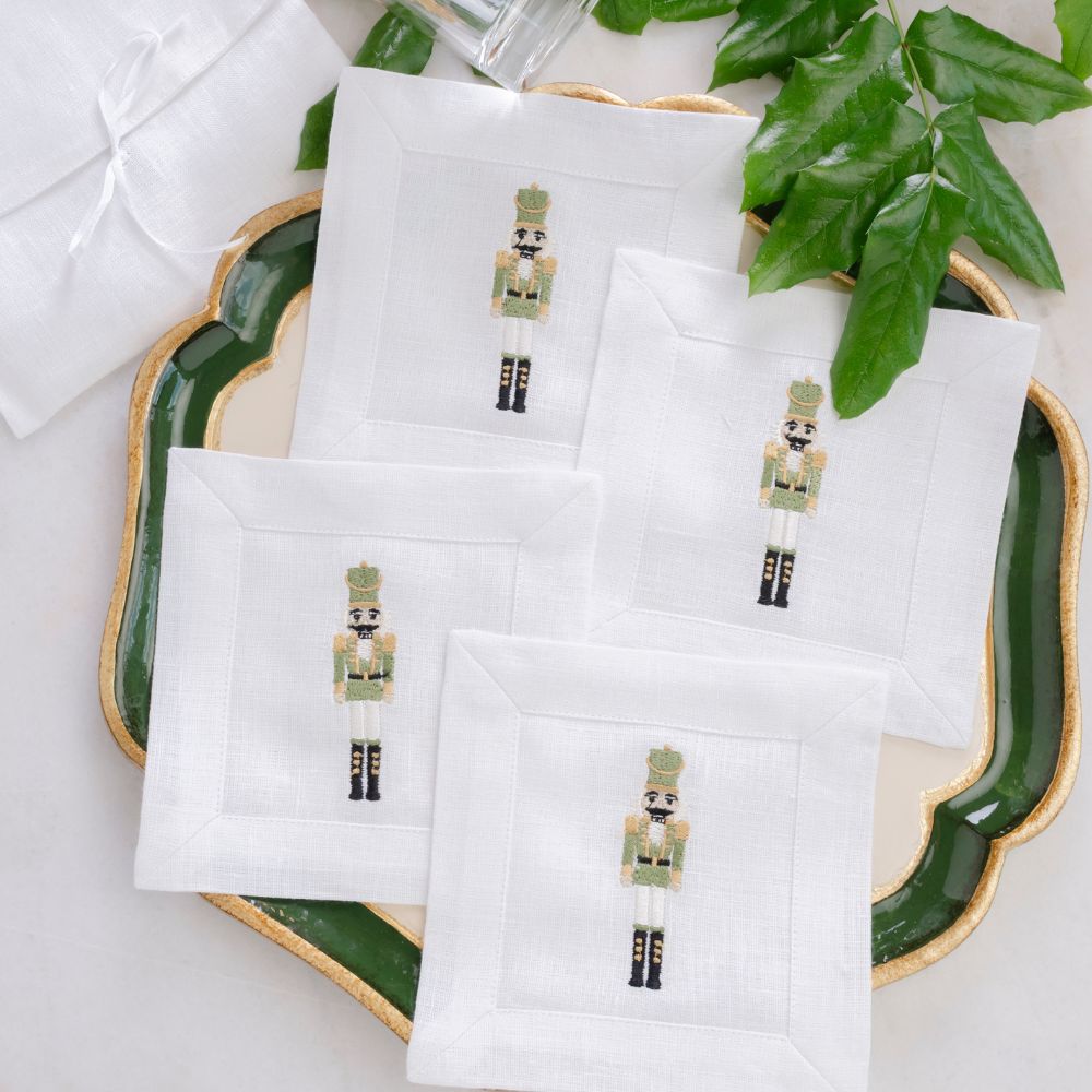 Set of white napkins with embroidered nutcracker designs on a decorative plate with green leaves.