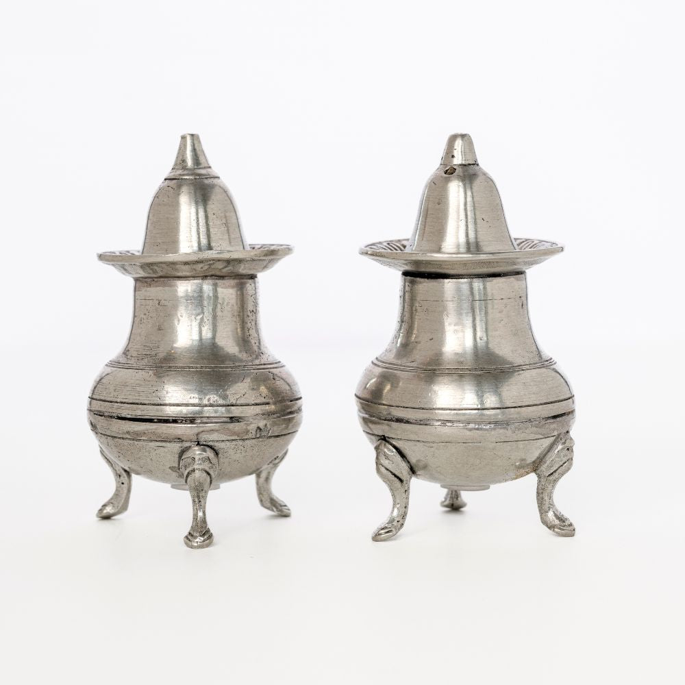Two pewter metal salt shakers with conical lids on a white background