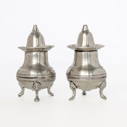 Two pewter metal salt shakers with conical lids on a white background