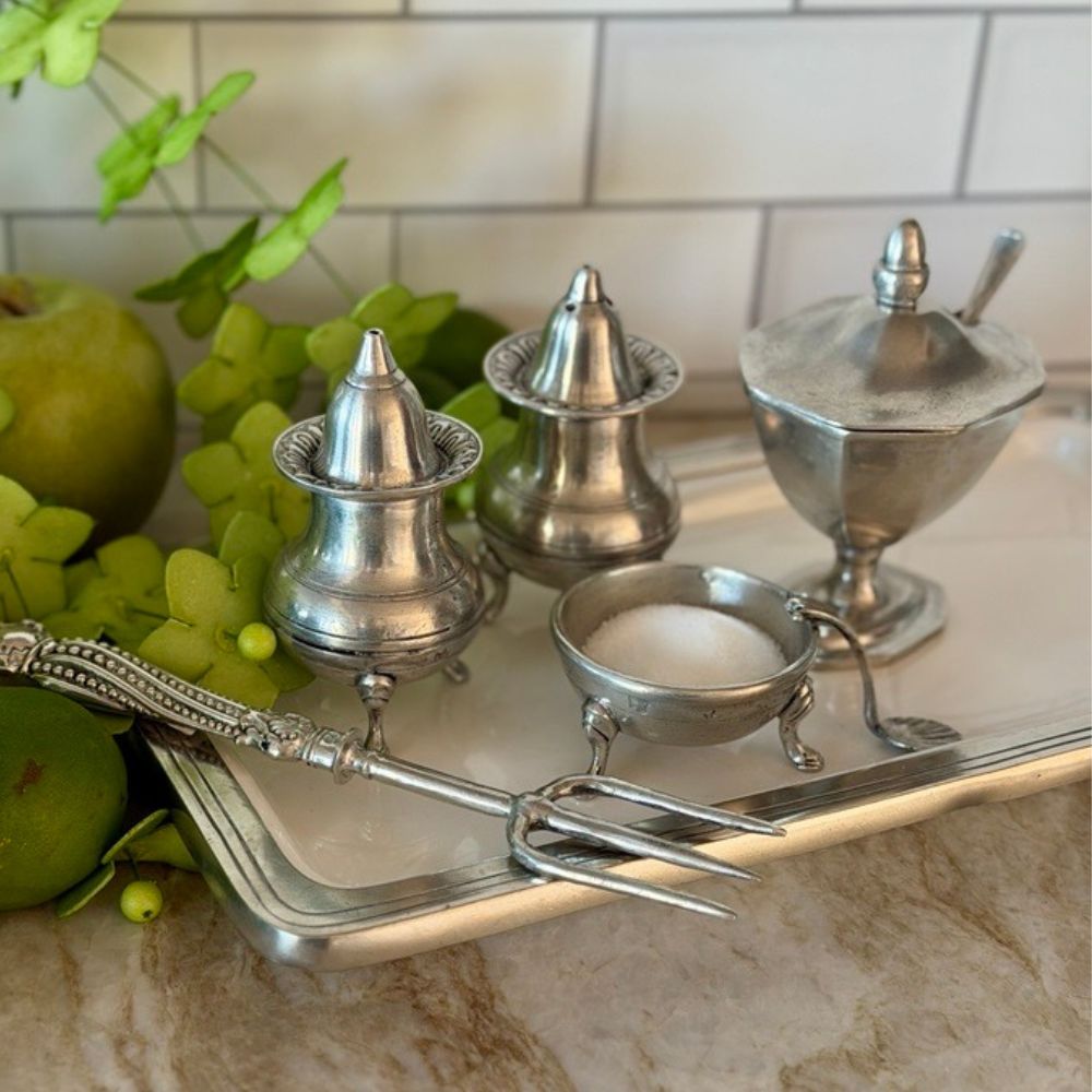 Set of pewter condiment containers on a tray with green apples and leaves.