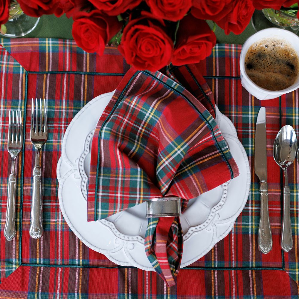 Plaid table setting with red roses, white plates, and silverware on a plaid tablecloth.