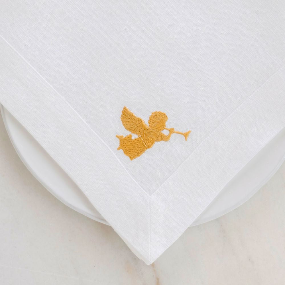 White linen napkin with gold angel embroidery on a beige background