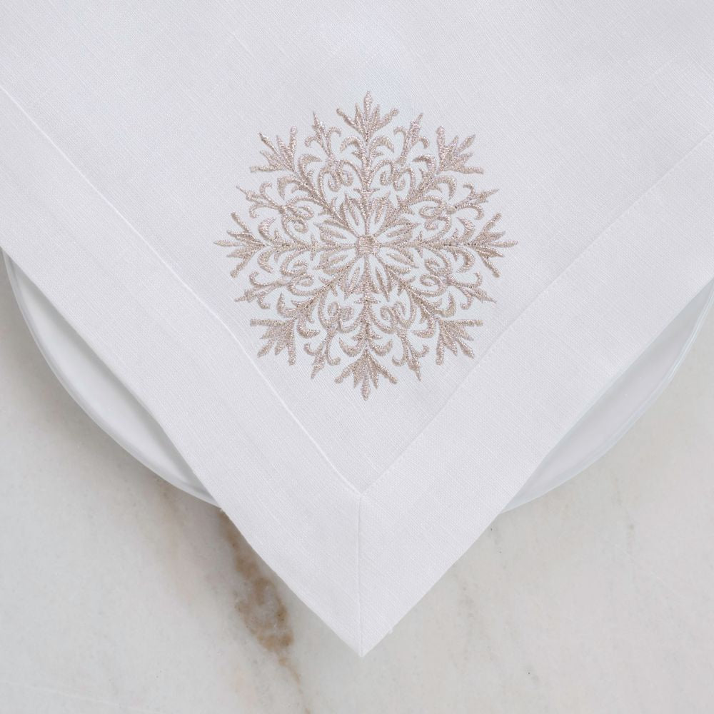 White linen napkin with a gold embroidered snowflake design on a light background