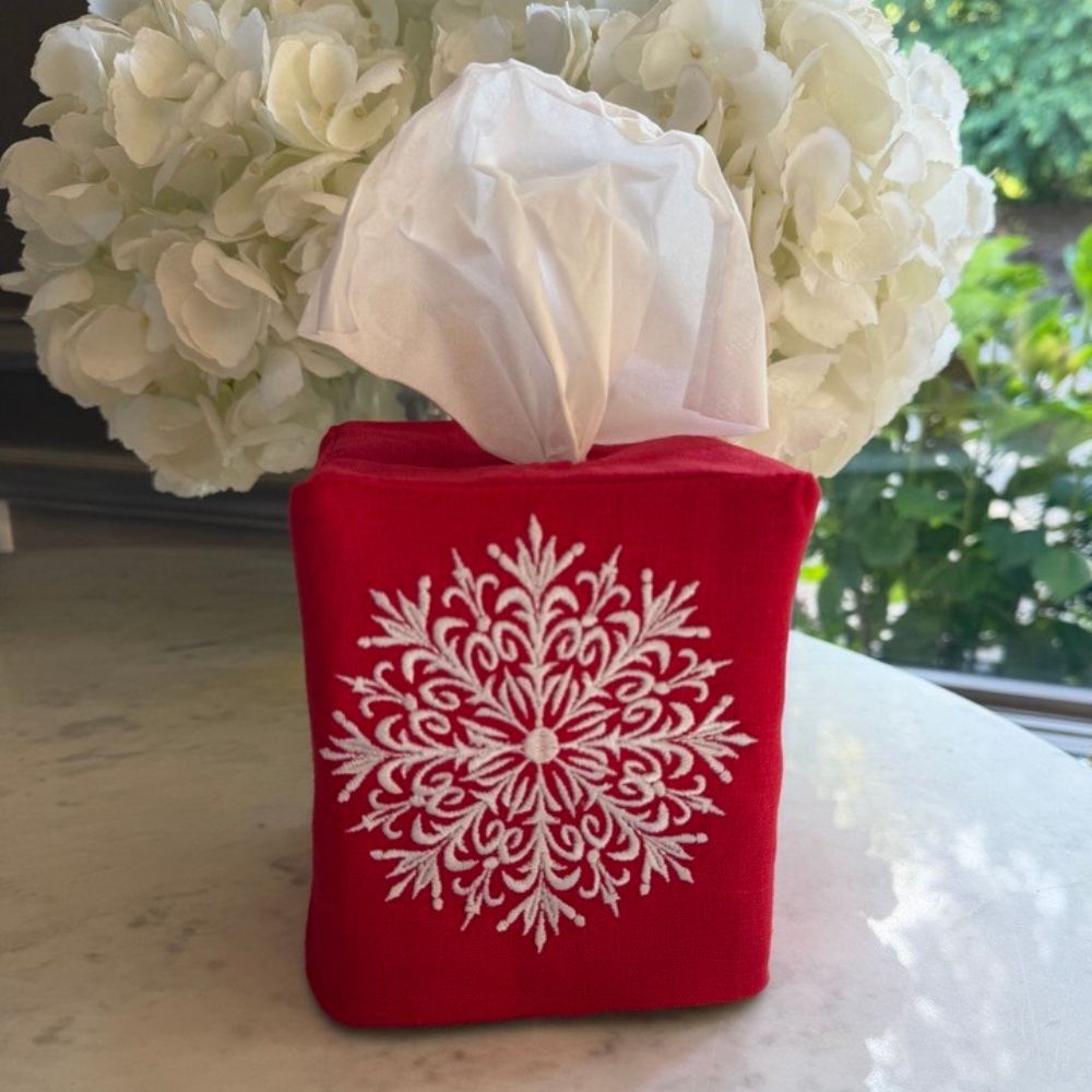 Red tissue holder with snowflake design on a table with white flowers in the background