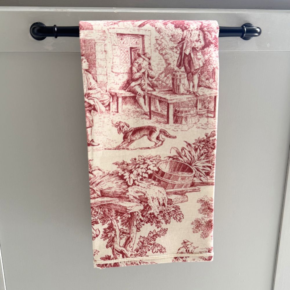 Decorative red and cream towel with vintage design hanging on a black towel rack against a gray background