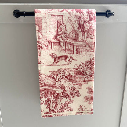 Decorative red and cream towel with vintage design hanging on a black towel rack against a gray background