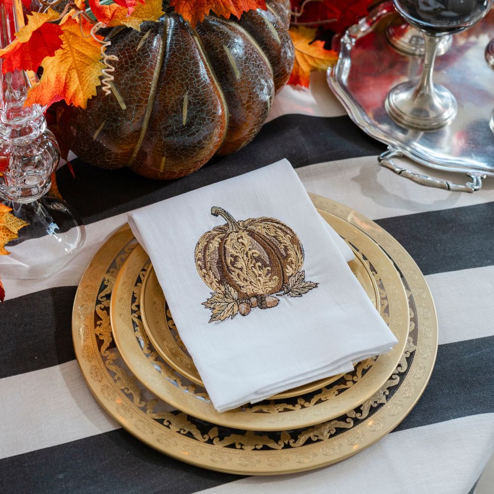 Table setting with pumpkin-themed towel and plates on a black and white striped tablecloth.