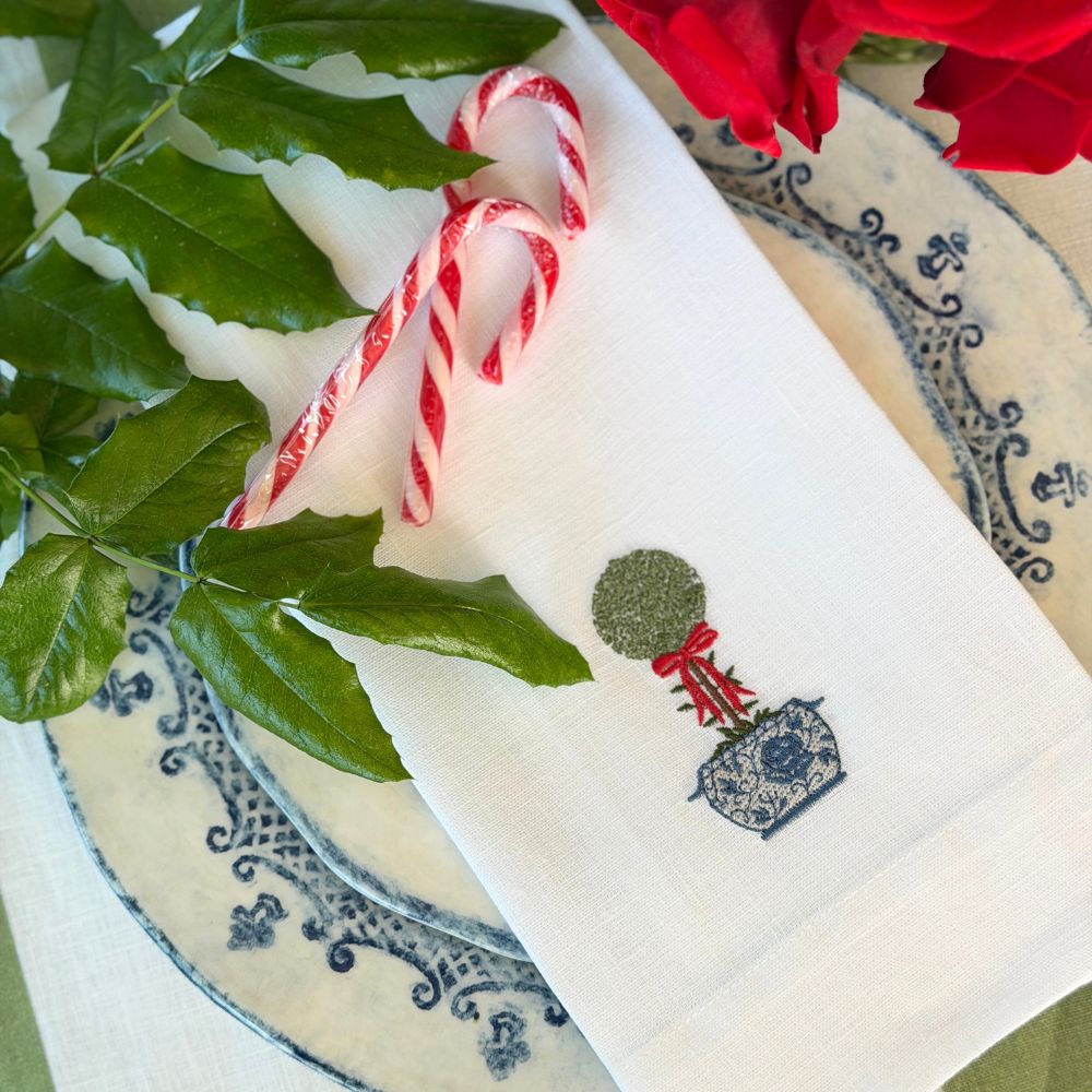 Linen towel with embroidered design featuring candy canes, greenery, and red flowers on a decorative plate.