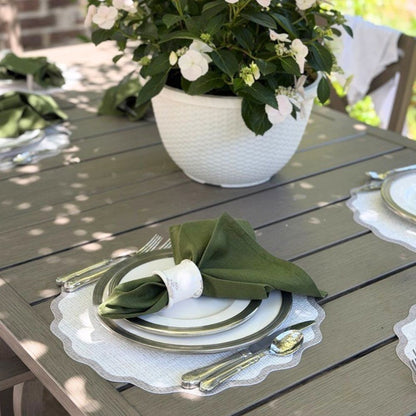 Outdoor table setting with green napkin, white plates, and silverware on a wooden table.