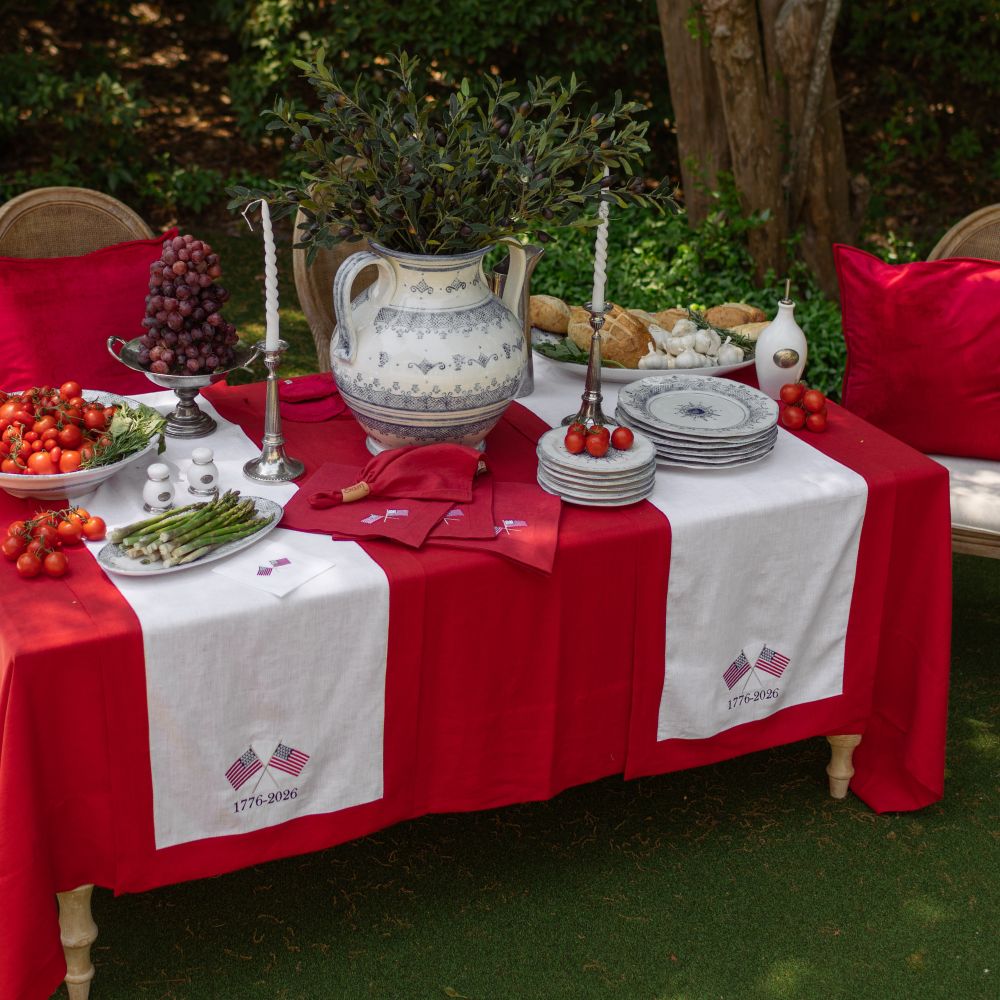 Decorative table setting with red and white tablecloth, food, and decorative items outdoors.