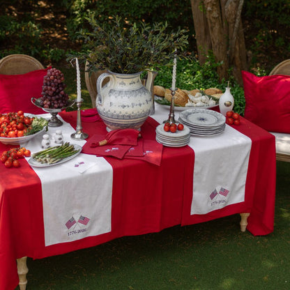 Decorative table setting with red and white tablecloth, food, and decorative items outdoors.