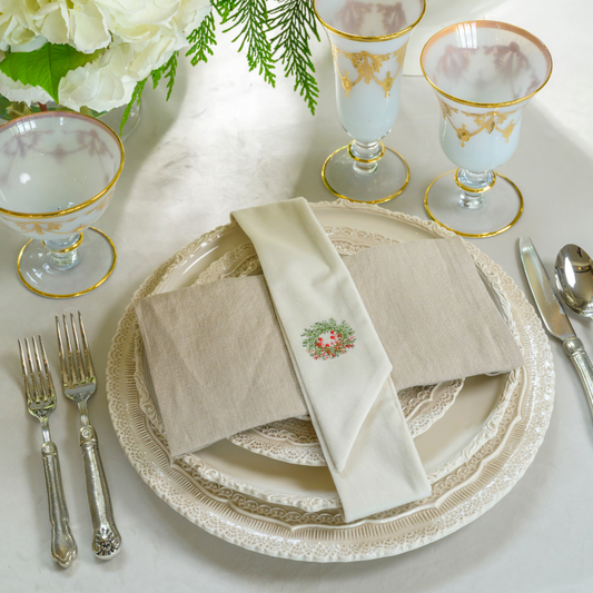 Elegant table setting with decorative napkin, wreath designed napkin sash, plates, and glasses on a white surface.