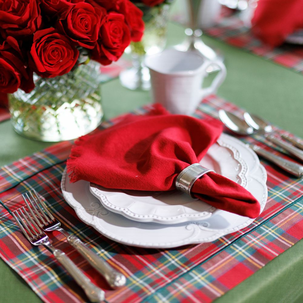 Table setting with red napkin, white plates, and silverware on a plaid placemat.