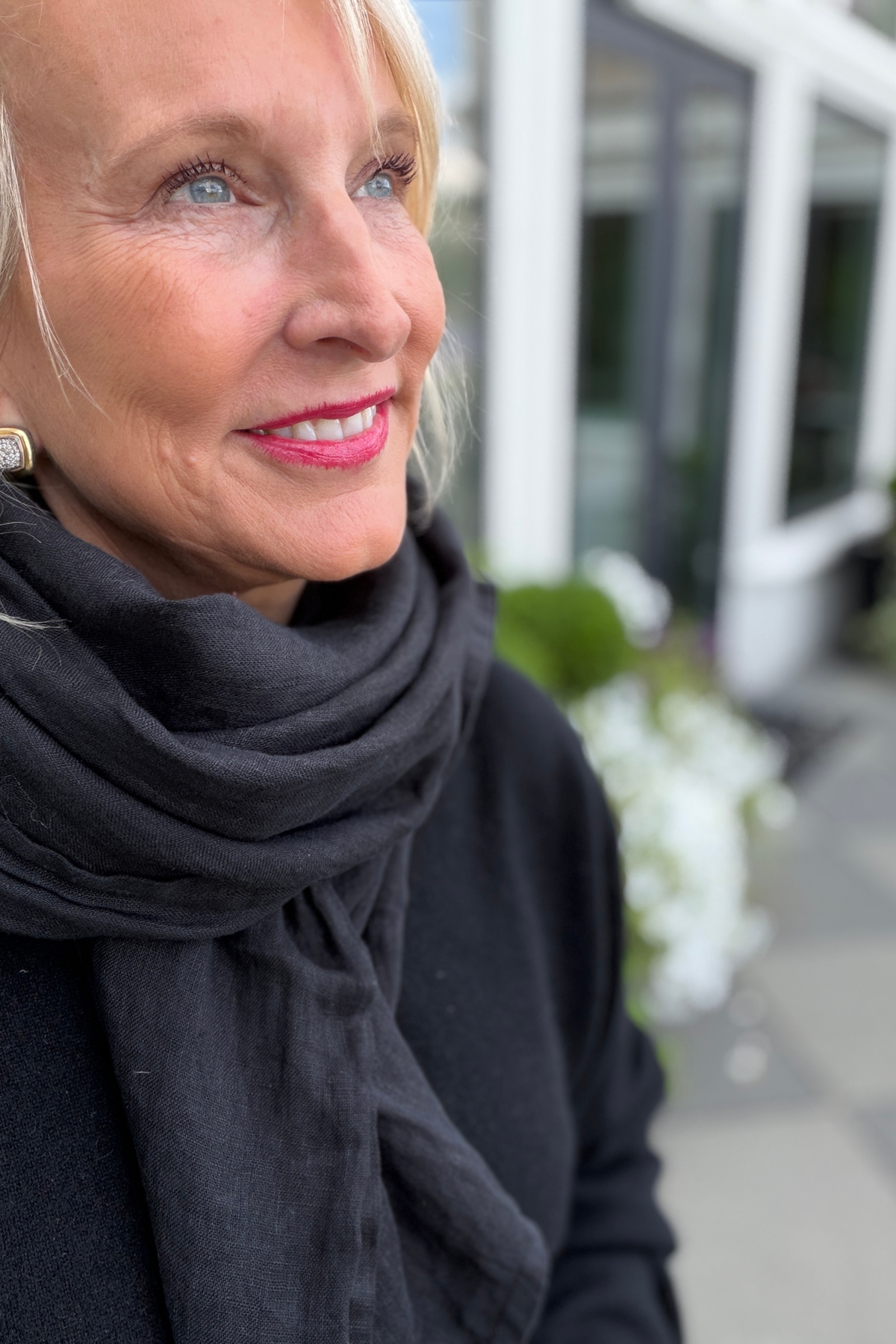 Close-up of black linen Stevie scarf draped around the neck, styled with a black top in an outdoor setting