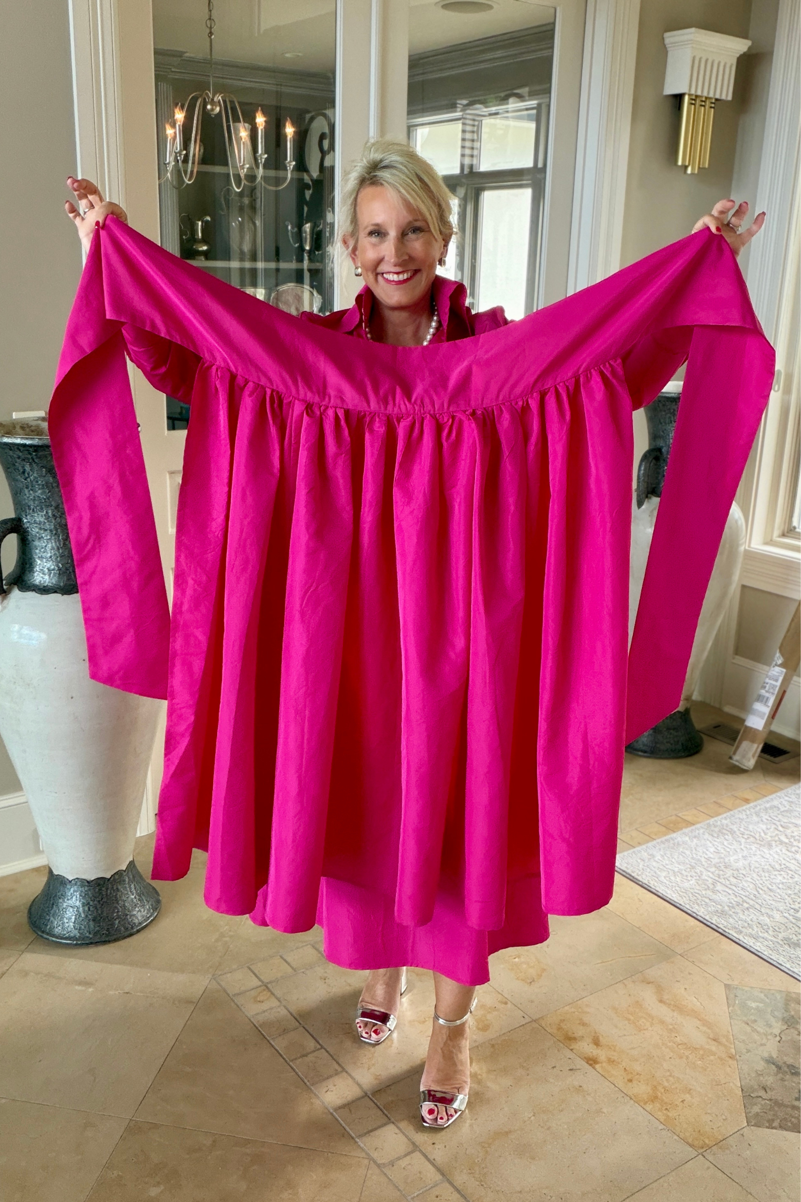 Fuchsia taffeta sash overskirt held up to show the gathered waistband and dramatic full skirt length, styled with a pearl necklace and silver heels in an elegant foyer