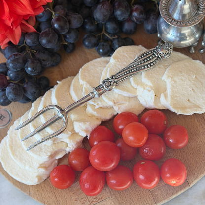 A Tavola pewter bread fork on a wooden cheese board with mozzarella tomatoes and grapes