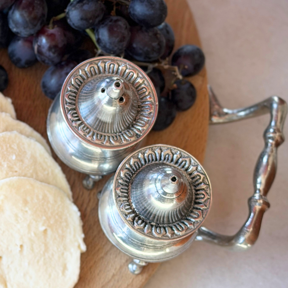 Top view of the Tavola pewter salt and pepper shakers showing rim decorative detail on a wood board with grapes and cheese