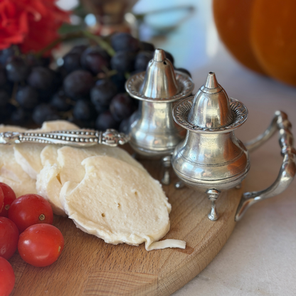 Set of pewter Tavola salt and pepper shakers with feet sitting on a wooden board with fruit and mozzarella