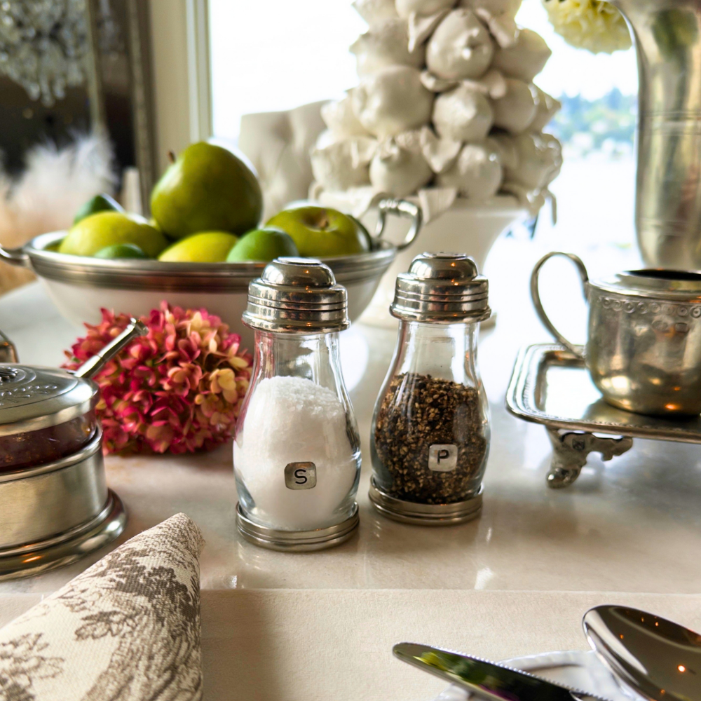 Tavola glass and pewter salt and pepper shakers on a white table with fruit in background