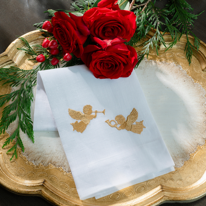 A white linen hand towel embroidered with trumpeting cherubs on a Florentino Gold Wooden tray with roses and greenery