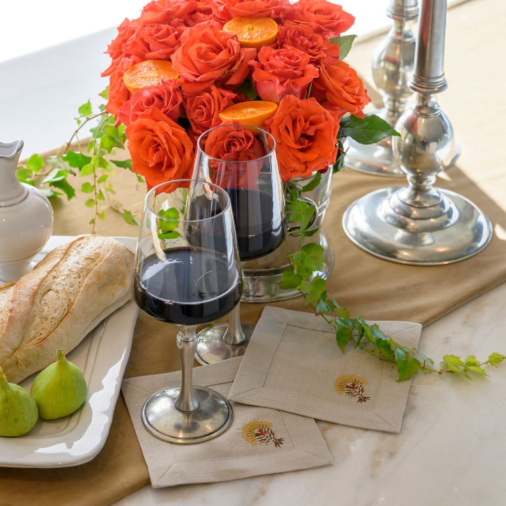 Table setting with red wine glasses, bread, figs, and a floral arrangement.