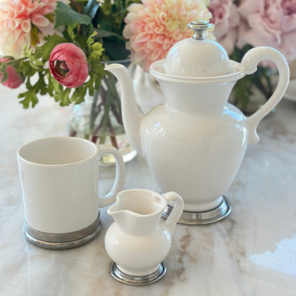 A Tuscan ceramic mug on a marble table with a Tuscan ceramic teapot and a piccolo pitcher