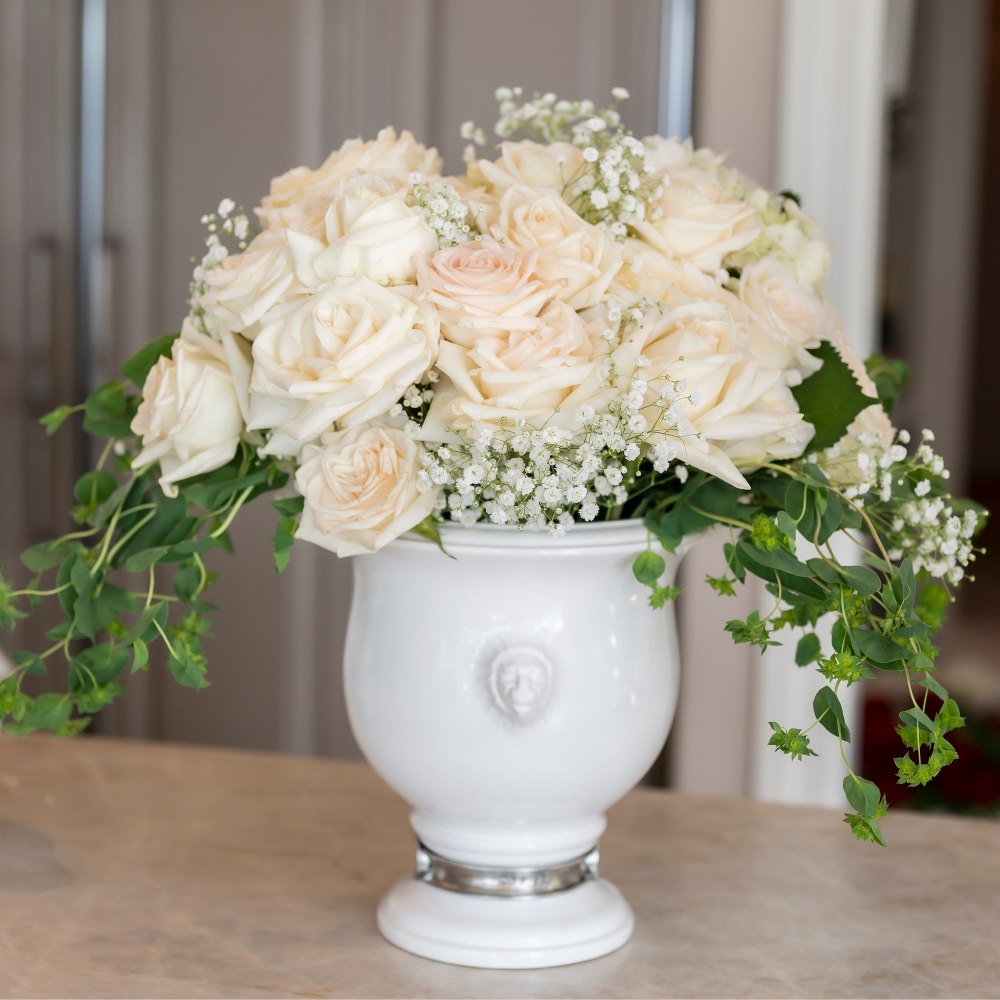 A Tuscan Lion Ceramic urn with an arrangement of blush roses and green leaves sitting on a counter
