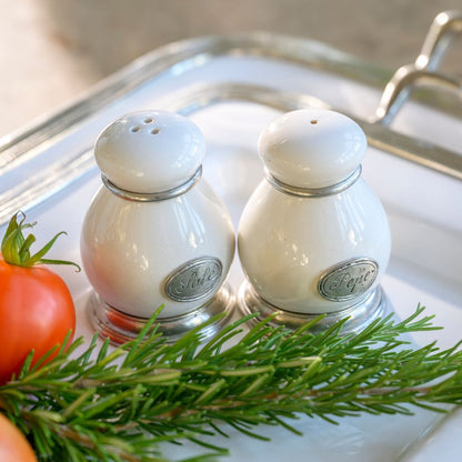 Two white ceramic salt and pepper shakers on a Tuscan tray with a tomato and rosemary sprig.
