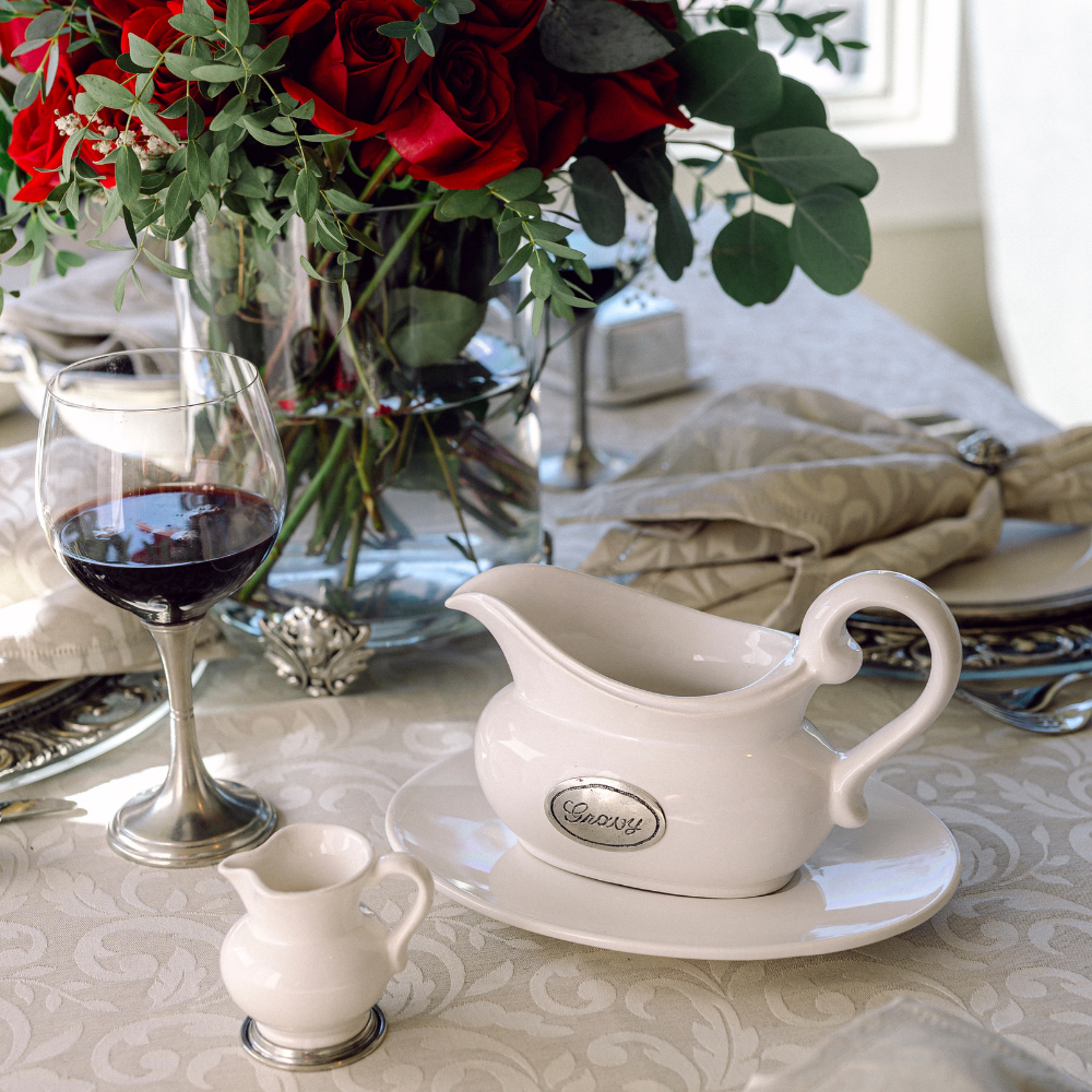 White gravy boat with a glass of red wine and floral arrangement on a table.