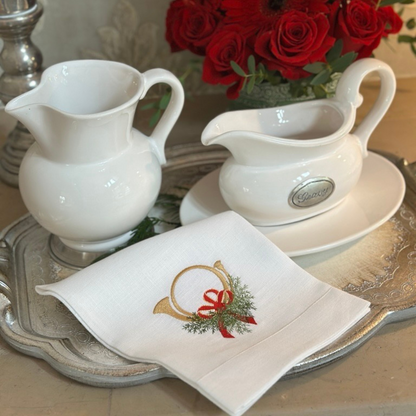 White ceramic Tuscan pitcher and gravy boat with saucer on a Florentino silver tray with a decorative napkin featuring a Christmas Horn with bow.