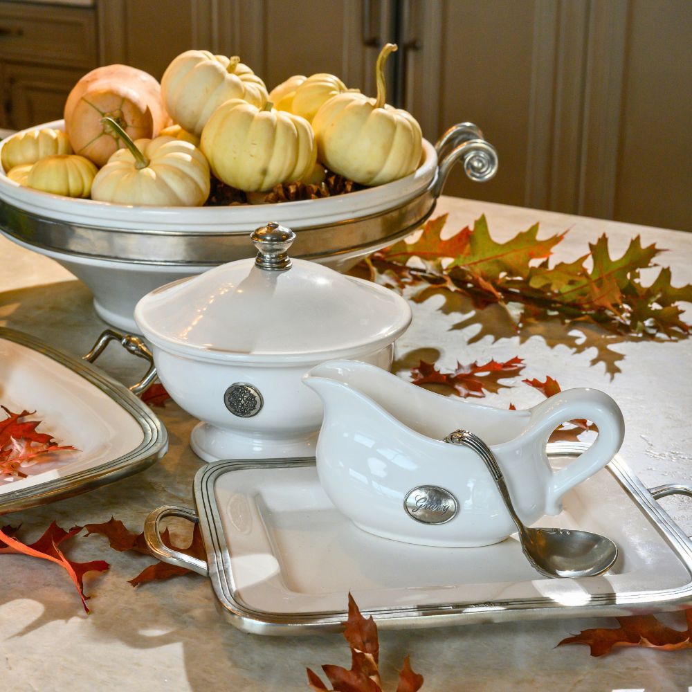 White ceramic gravy boat and tureen with lid on a table with pumpkins and fall leaves.