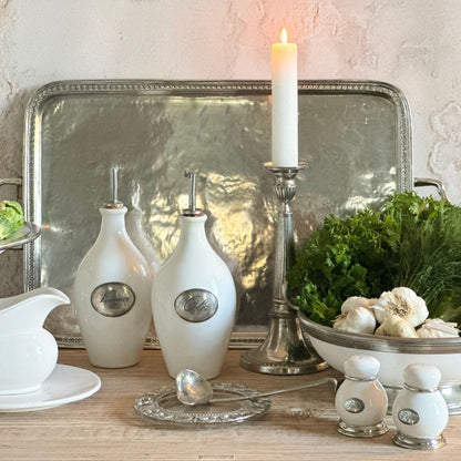 Decretive setting with Tuscan white oil and vinegar bottles, pewter candlestick holder, and greenery on a wooden surface.