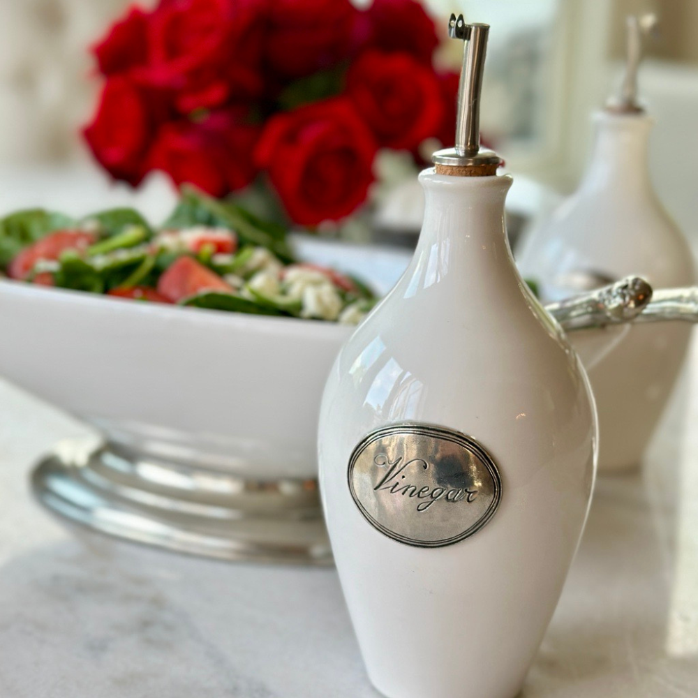 Close up detail shot of a white ceramic vinegar bottle with spout on a table with salad