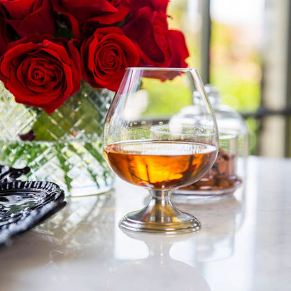 Side view of Arte Italica Verona Cognac Glass showing wide bowl and Italian pewter stem on white counter with red roses
