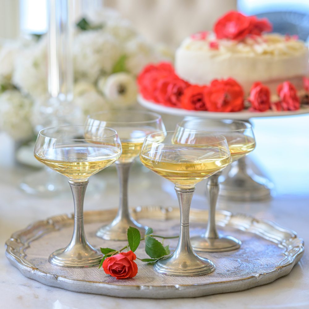Verona coupe glasses on a silver tray filled with sparkling wine with a cake in the background