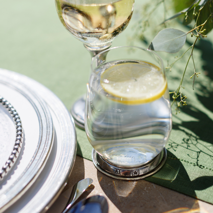 A Verona glass tumbler with a pewter base filled with water and a lemon on a green linen runner next to Tuscan plates