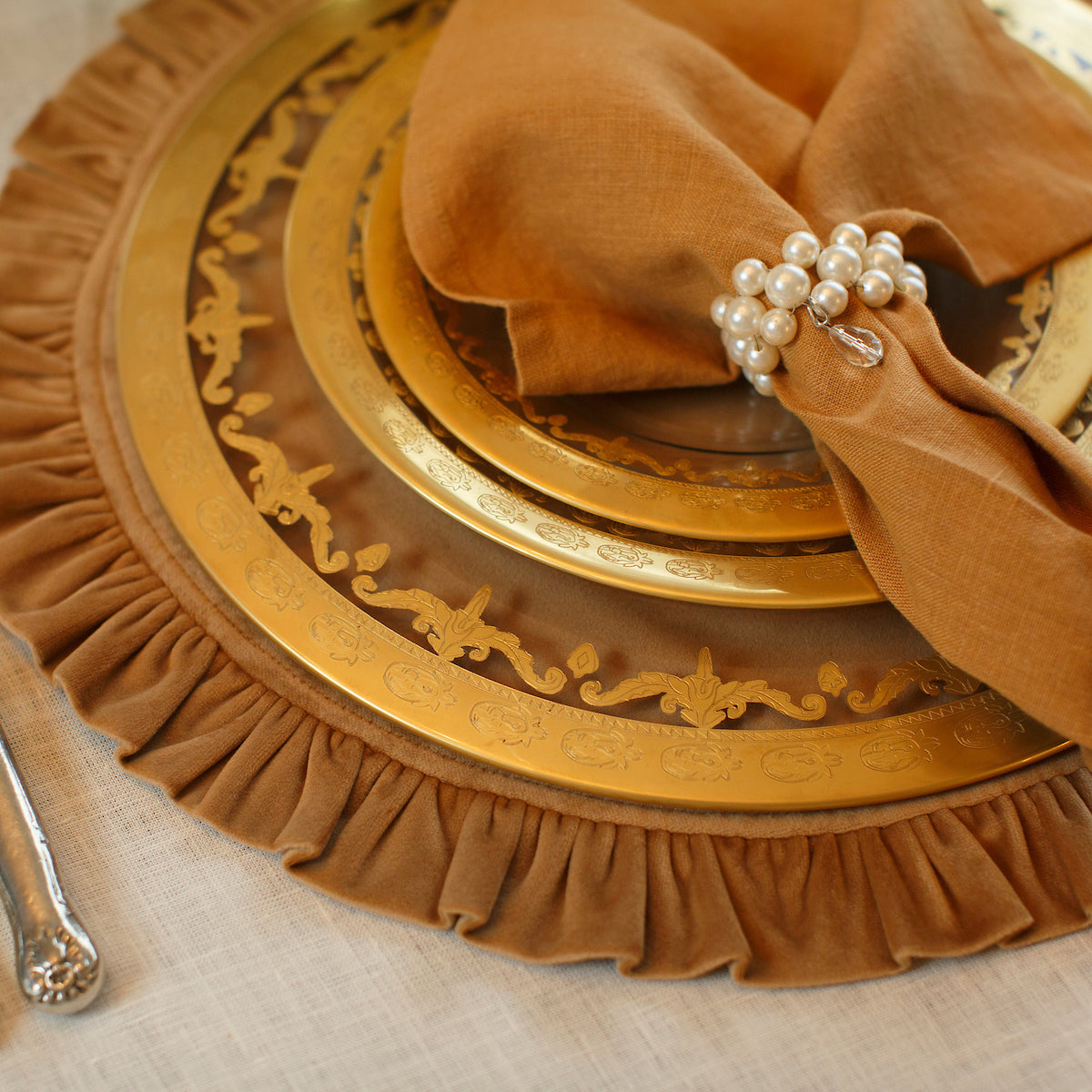 Vetro Gold Charger with burnt orange accent pieces and an orange napkin with a pearl napkin ring