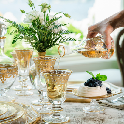 Hand pouring wine into a Vetro Wine Glass from a Small decanter on a table set with the Vetro Gold Collection