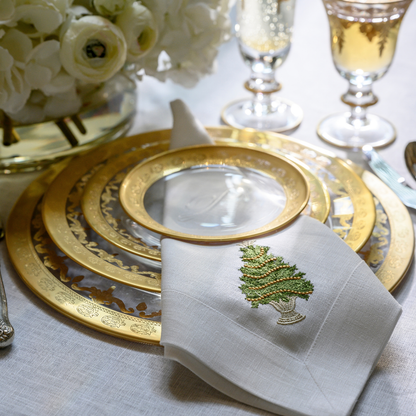 Vetro Gold glass charger styled with dinner, salad, and bread plates, with a white tree with gold trim embroidered napkin on a table