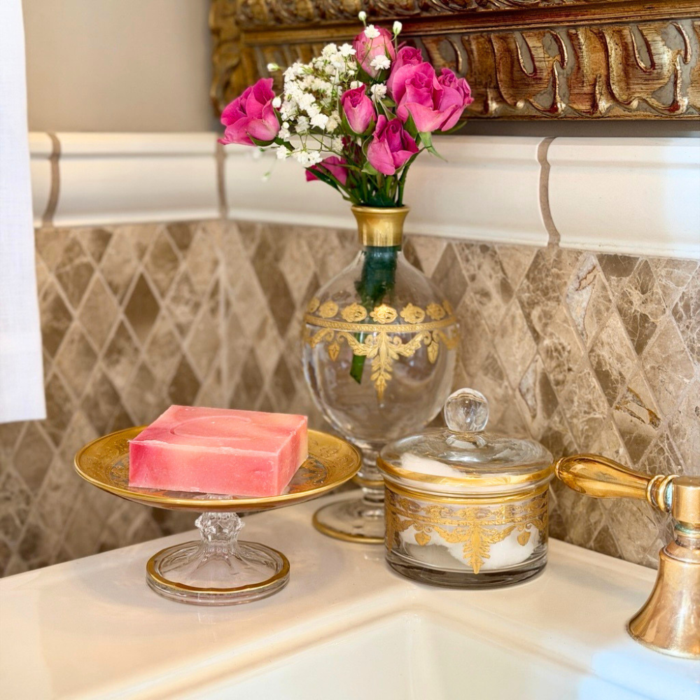 Vetro gold patisserie dish used as a soap holder with a covered dish holding cotton balls with a bud vase on the side of a sink